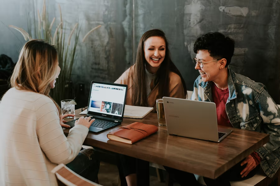 A small group of three people sit together at a table working on their laptops for virtual fundraising ideas.