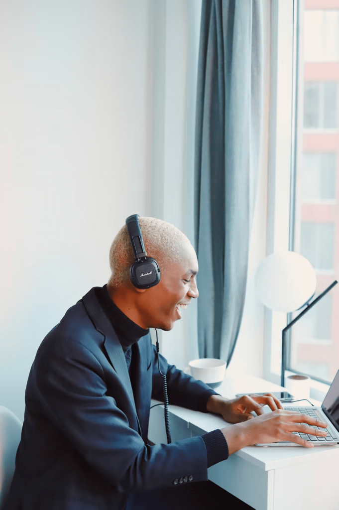 A young man dressed in a blazer and turtleneck sweater wears headphones as he sits at his laptop while attending a nonprofit virtual fundraising event.