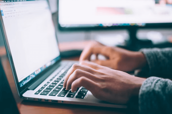 Two hands type on a laptop keyboard in a home office setting.