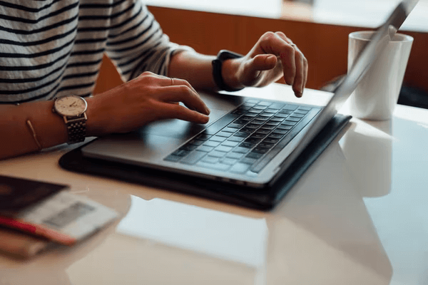 Two hands reach out to type on a laptop keyboard at a coffee shop table.