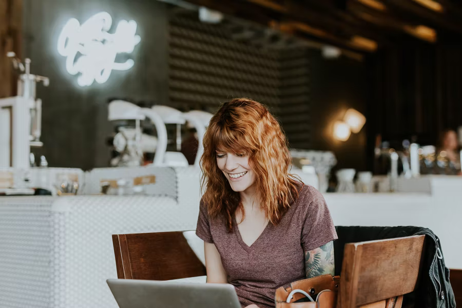 A woman with red hair sits at her laptop, smiling after she donates to a nonprofit online.