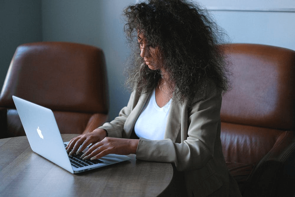 A young woman sits in a leather chair at a small table to work on collecting nonprofit data on her laptop.