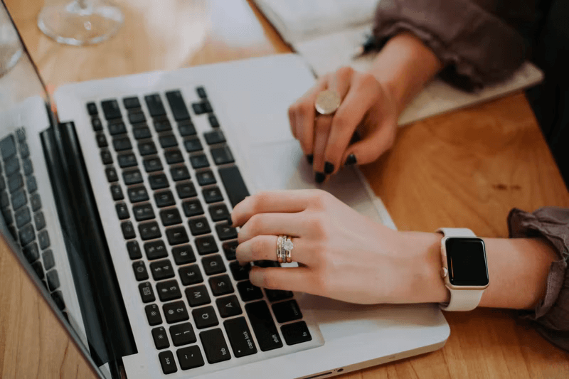 A young woman reaches out to type on her laptop keyboard.