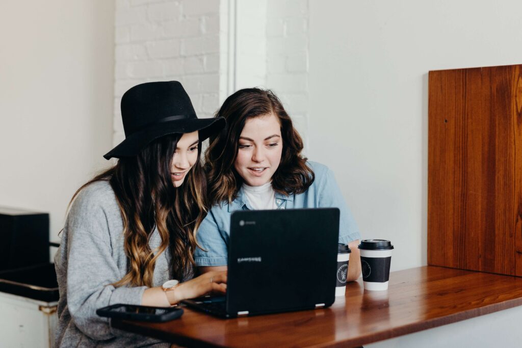 Two millennial women sit at a computer with coffee cups as they provide their millennial support to nonprofits. 