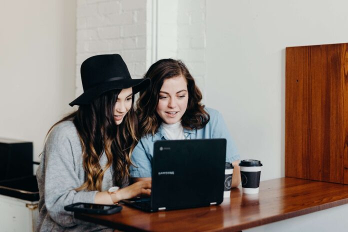 Two millennial women sit at a computer with coffee cups as they provide their millennial support to nonprofits.