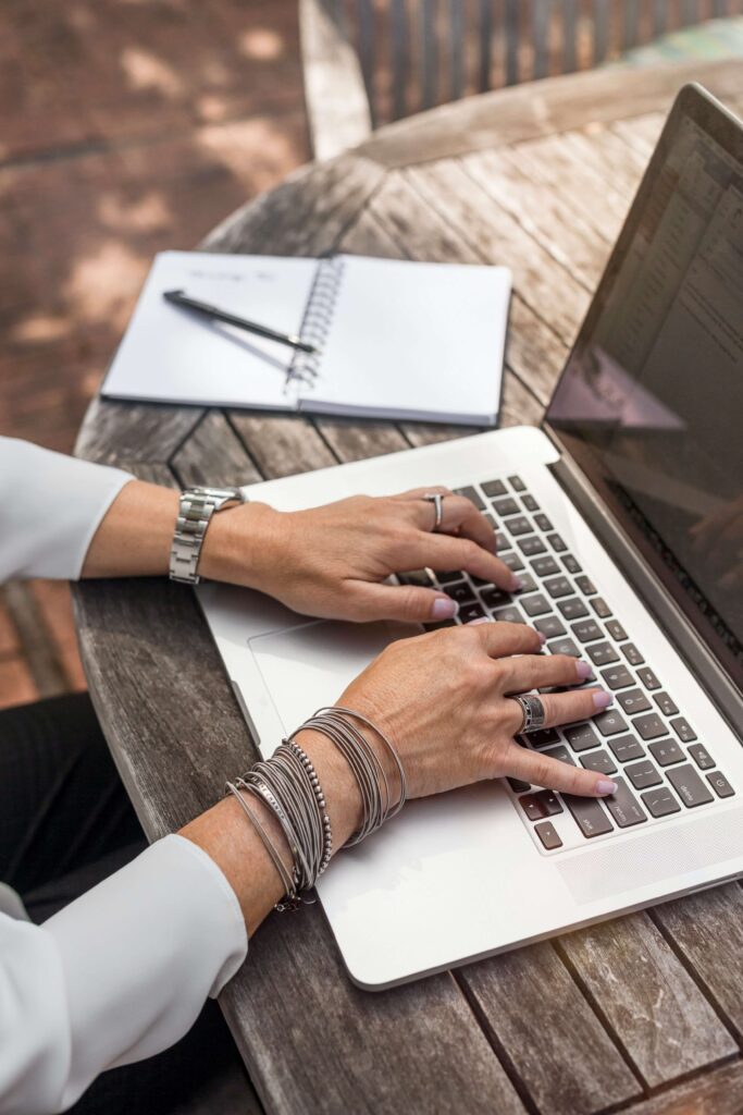 A person sits at a table to work on her laptop, where she pulls up Bloomerang for her nonprofit.